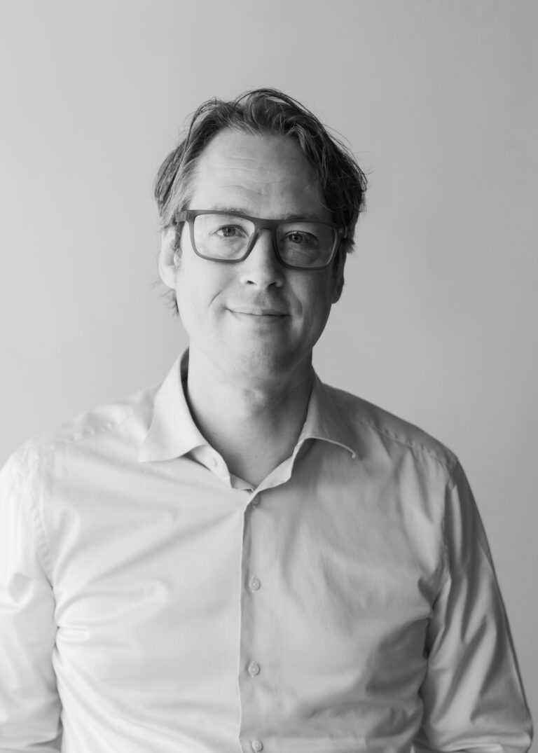 Professional portrait of a man with glasses in a white shirt.